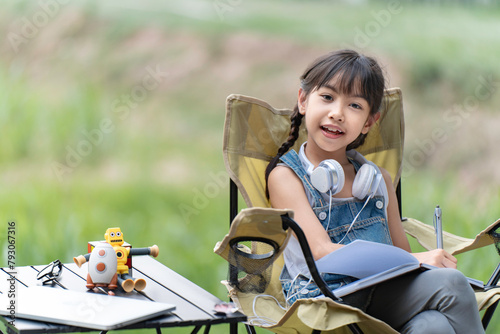 A little girl is sitting and writing, doing homework in the garden in nature.