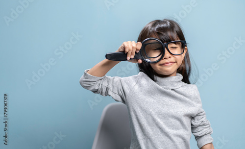 A little girl is holding a magnifying glass for studying.