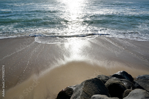 Waves roll onto the sandy sea beach. Stone blocks lie on the beach