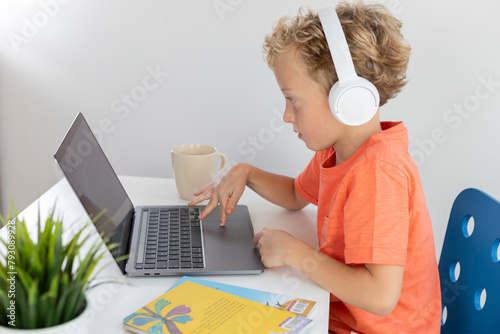 Little boy with headphones and blonde hair plays with a laptop