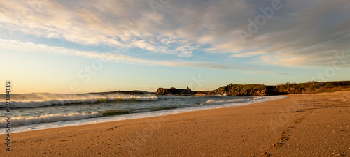 Foxos beach, Sanxenxo (Spain). Golden sand beach bounded by rocks. Late afternoon golden light and waves crashing against the sand
