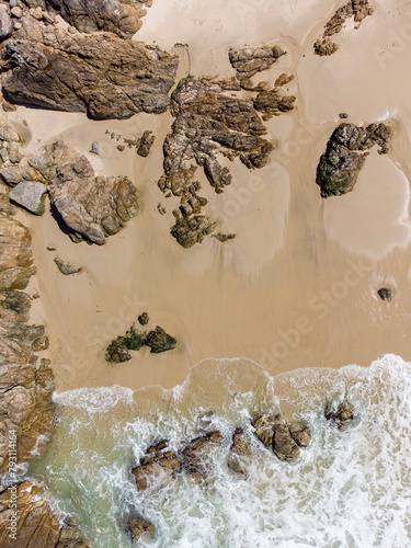 Aerial view. Detail of a beach with golden sand and rocks, with a wave entering the photo