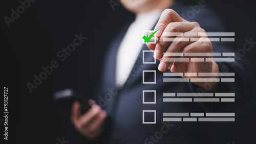 A man is holding a smartphone and use a digital pen to check a green check mark on checkbox on screen. Quality control and satisfaction checking the checklist concept.