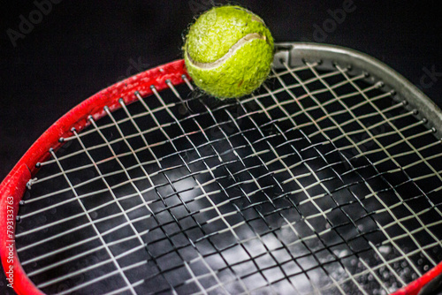 Green tennis ball on a red tennis racket close-up on a black background with white scattered powder