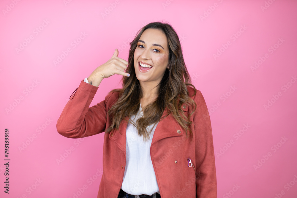 Young beautiful woman wearing casual jacket over isolated pink background smiling doing phone gesture with hand and fingers like talking on the telephone Young beautiful woman wearing casual jacket over isolated pink background smiling doing phone gesture with hand and fingers like talking on the telephone