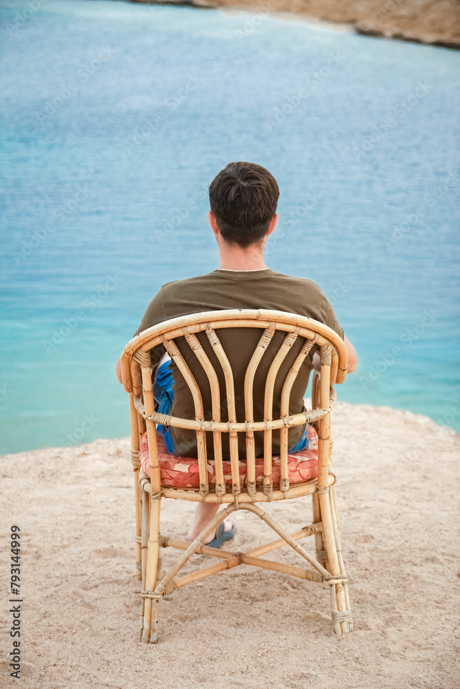 Happy guy sitting on a stool by the sea background on the nature - obrazy, fototapety, plakaty 