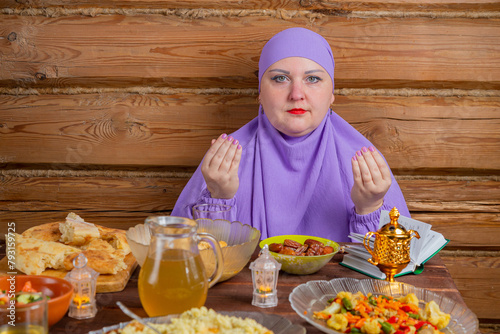 A Muslim woman in a lilac hijab at the table begins a meal, the holiday of Eid al-Fitr says bismi llah