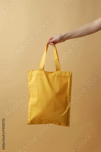  Person's hand holding a yellow shopping bag against beige backdrop Another hand lifting same-colored bag