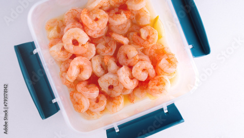 Boiled peeled king prawns in a plastic container on a white background close-up.