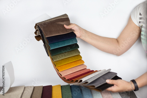 A woman is holding a catalog with fabric samples in her hands, a woman is choosing a fabric for her new sofa, the focus is on her hands and on the fabric