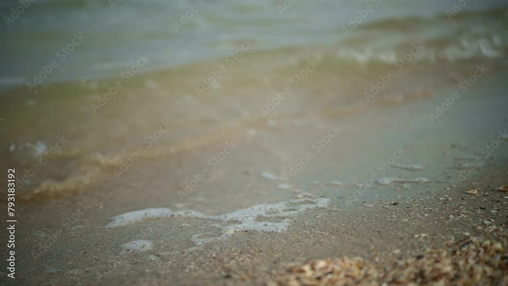 Slim female legs and feet walking along sea water waves on sandy beach. Pretty woman walks at seaside surf. Splashes of water and foam