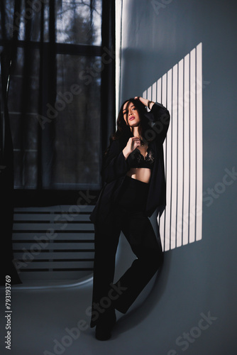 A pretty woman in a black satin suit. Stylish woman in a suit against the background of studio lighting