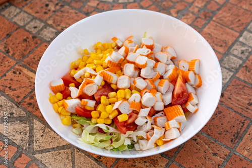 Obraz na płótnie On a white plate, there's a multi-hued salad adorned with crab sticks, corn, and fresh green lettuce, enticing the appetite w salonie