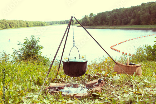Cooking soup in a cauldron over an open fire in nature. bonfire on the shore of the lake. A cast iron pot on a fire against the background of a river.