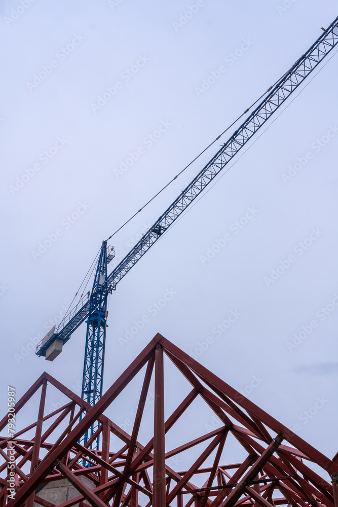 Geometric composition of red metal beams and a blue crane in a modern construction against a clear sky. Geometric composition of red metal beams and a blue crane in a modern construction against a clear sky.
