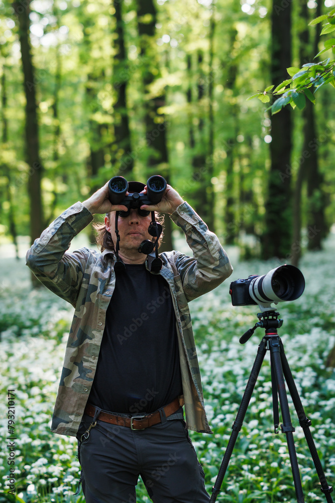Wildlife photographer is bird watching in forest. Man with binoculars looking for birds in spring woodland