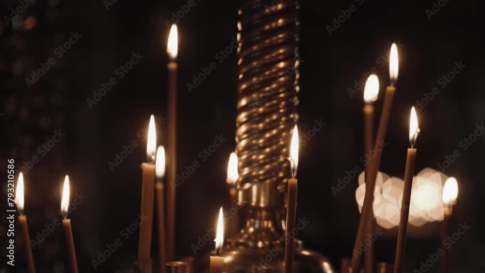 Burning candles in the Orthodox church. Wax candles burn in the dark in church against dark. Church candles burn on a large gold candlestick in the church. Burning candles in the Orthodox church. Wax candles burn in the dark in church against dark. Church candles burn on a large gold candlestick in the church.