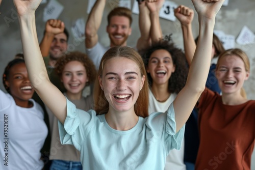 Portrait of happy young woman with arms raised celebrating success in office. Cheerful multiethnic group of people standing together. Success concept © Inigo