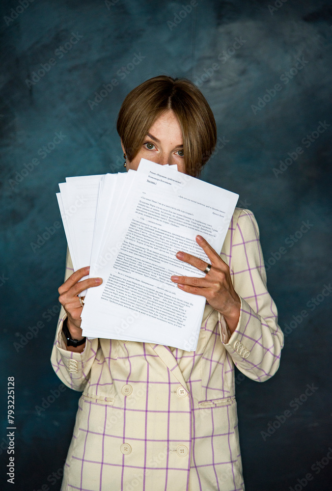 Fototapeta premium portrait of romantic smiling beautiful woman in white jacket staying on dark blue background and holding manuscripts in her hands. writer. Teacher. Education conception