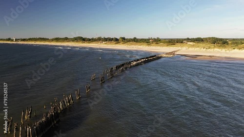 The old ruined breakwater pier is washed by strong waves. The shore in the red lighthouse