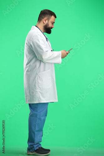 Male doctor, full-length, on a green background, with a phone
