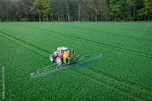 Pflanzenschutz im Ackerbau - roter Traktor mit Feldspritze im jungen Getreidebestand, Luftaufnahme.