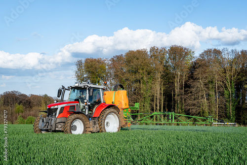 Pflanzenschutz im Ackerbau - roter Traktor mit Feldspritze im Getreidefeld  Frontansicht.