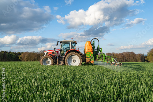 Getreideanbau - roter Traktor mit angebauter Feldspritze bei einer Pflanzenschutzma  nahme im Getreidefeld.