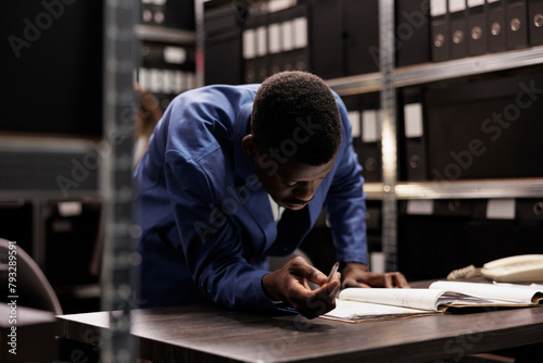 African american manager brainstorming ideas while working at accountancy research, analyzing bookkeeping report. Businessman searching for administrative record working overtime in arhive room.