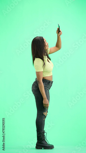A woman, on a green background, in full height, waving her phone