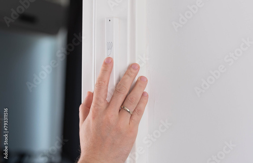 Hand gently touches the Jewish mezuzah on the doorpost, a prayer for home protection in Judaism. White interior, stylish modern mezuzah in Israel.
