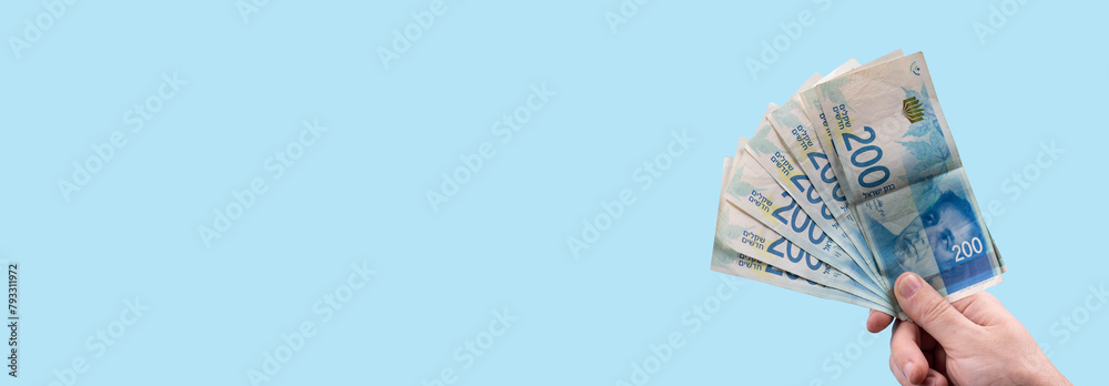 Hand holding stack of cash bills, New Israeli Shekels (NIS), representing financial wealth, abundance, and prosperity in Israel. - obrazy, fototapety, plakaty 