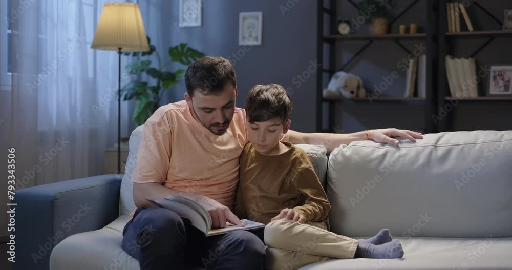 Happy family. Dad and son reading interesting book in the evening. Father and son leisure relax sitting on the sofa at home. Relationship, connection, bonding, fatherhood Happy family. Dad and son reading interesting book in the evening. Father and son leisure relax sitting on the sofa at home. Relationship, connection, bonding, fatherhood