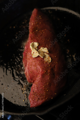 Red beef steak cooking in skillet on stove with butter and seasoning 