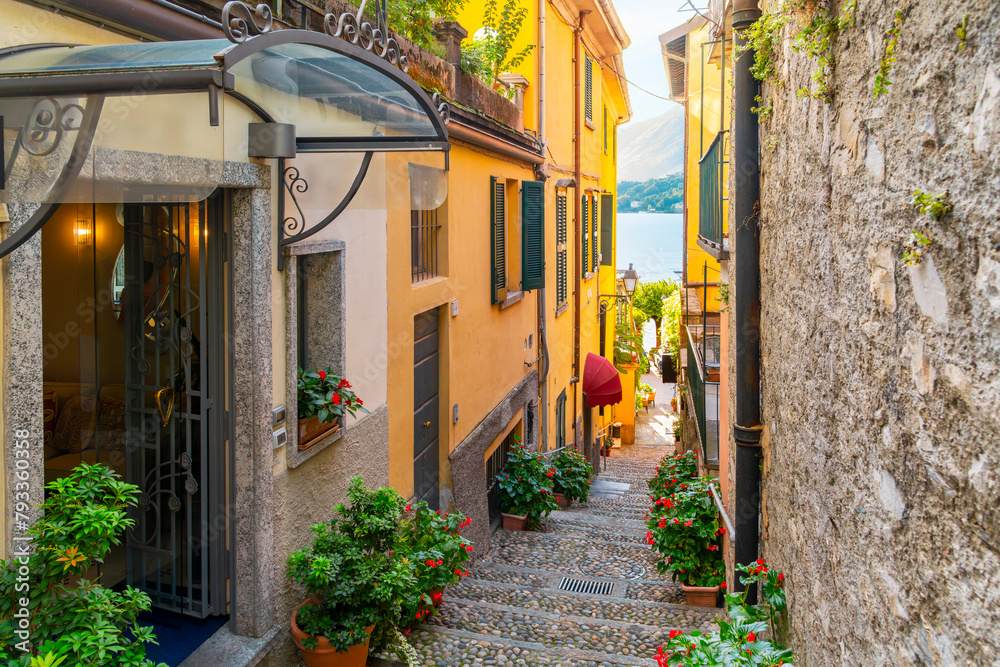 Fototapeta premium A narrow cobblestone alley with steps leading to the lake on a steep staircase with shops and cafes in the historic old town of Bellagio, Italy, on the shores of Lake Como.