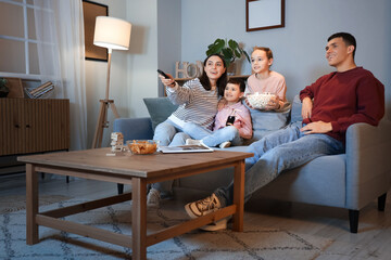Happy family with popcorn watching TV on sofa at home in evening