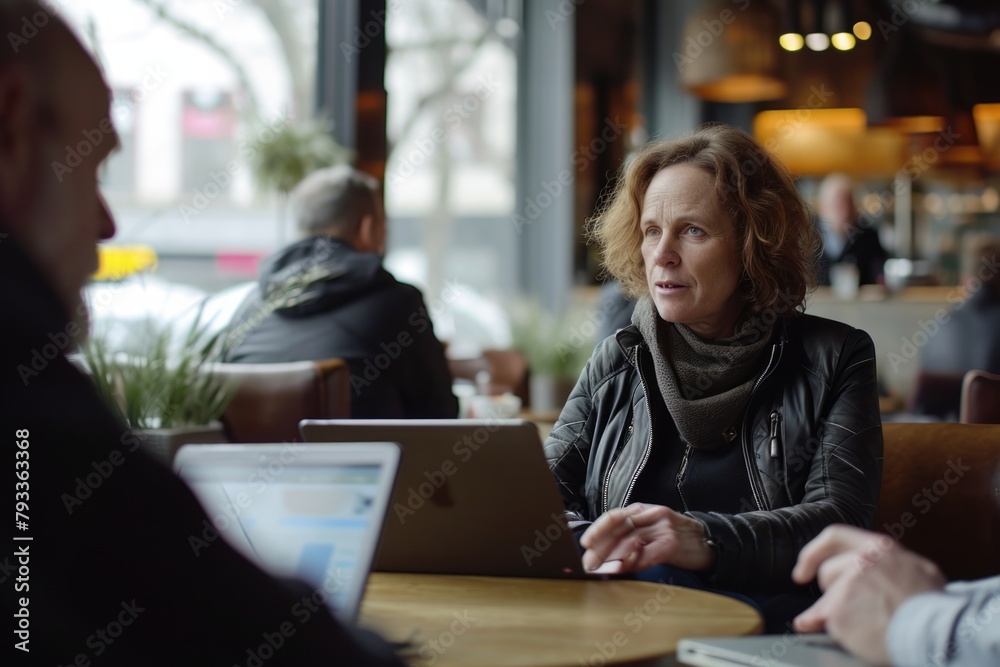Mature woman sitting in cafe and using tablet pc. Unrecognizable people on background.