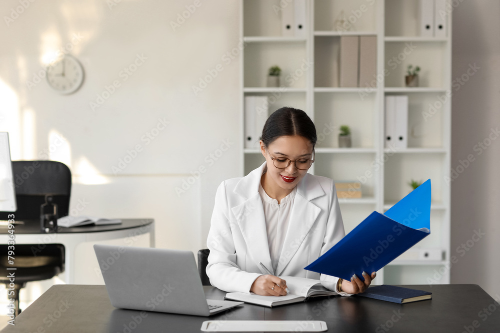 Young Asian businesswoman with folder working at table in office Young Asian businesswoman with folder working at table in office