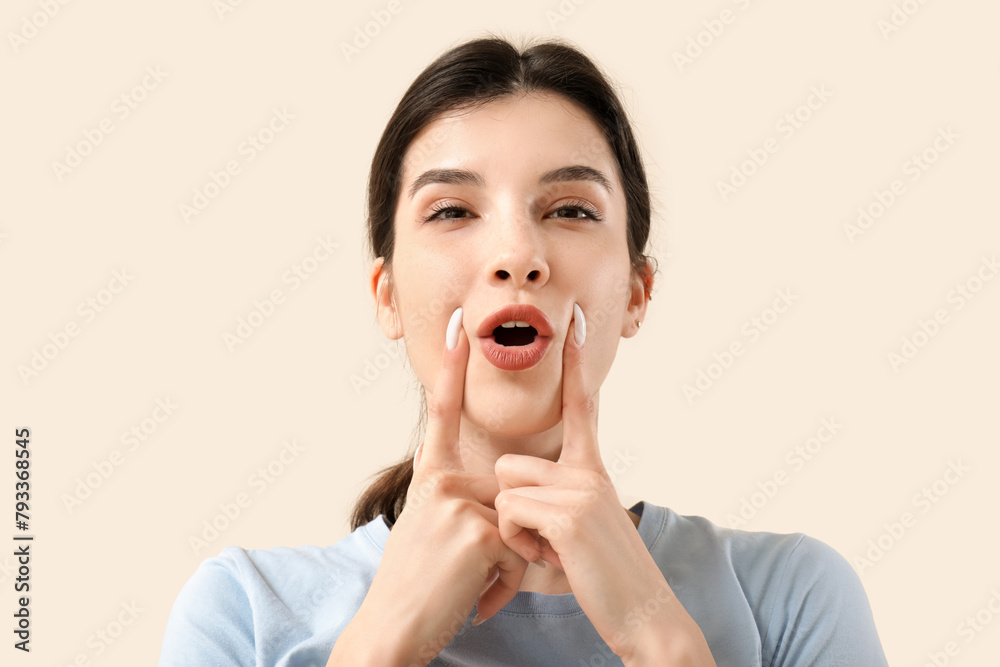 Beautiful young woman doing face building exercise on beige background Beautiful young woman doing face building exercise on beige background