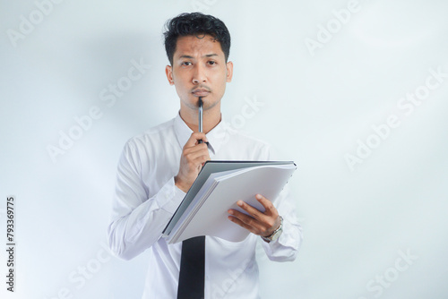 Young Asian business man showing thinking gesture while holding pen and note book photo