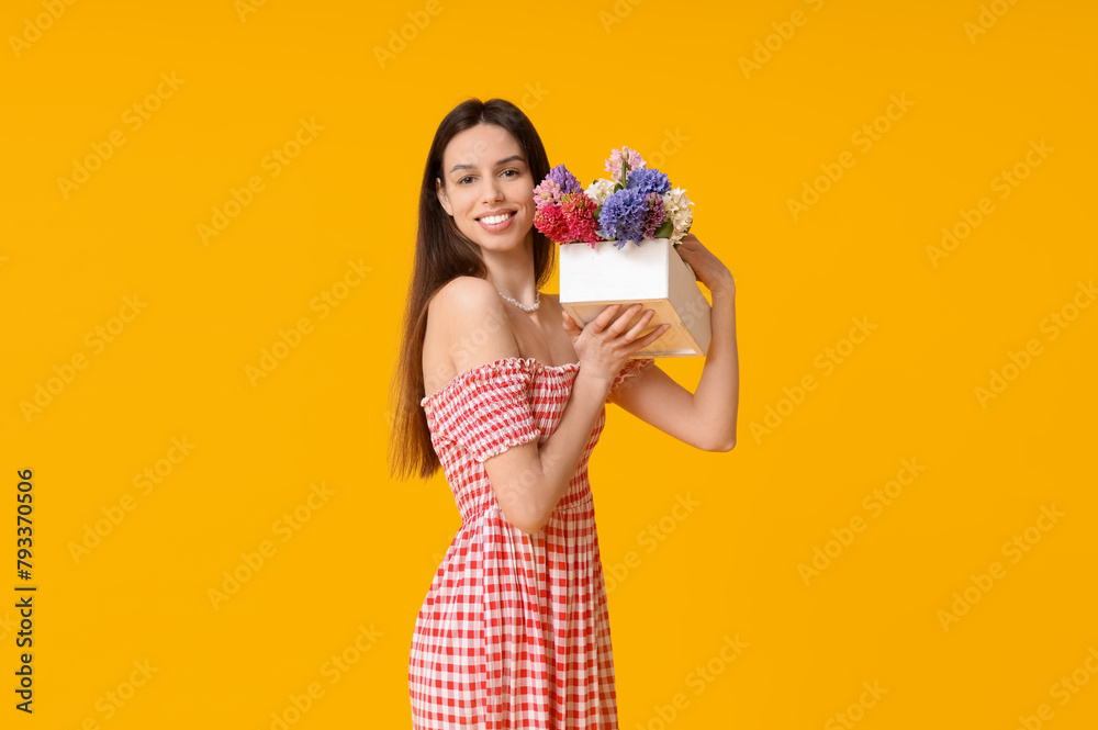 Happy smiling young woman holding basket with hyacinth flowers on yellow background Happy smiling young woman holding basket with hyacinth flowers on yellow background