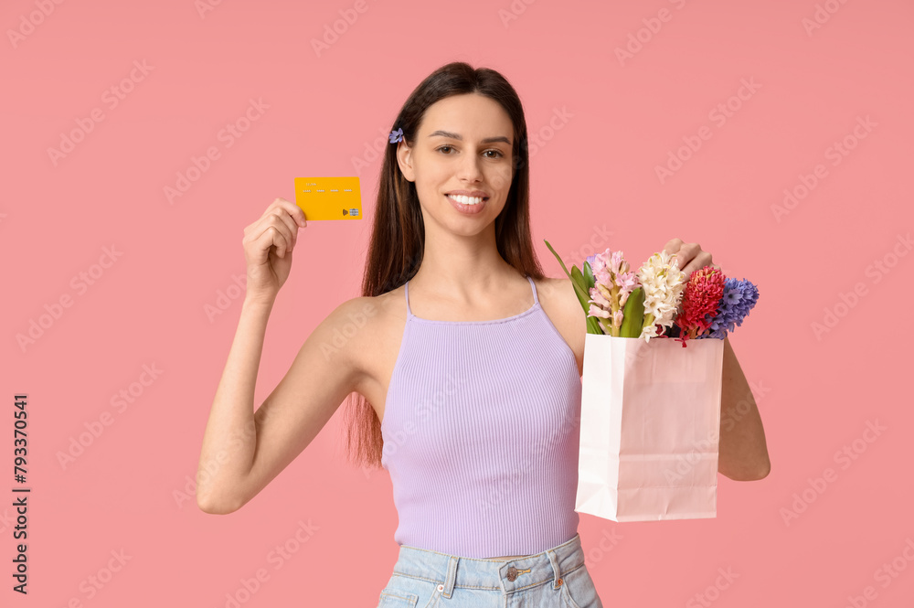 Happy smiling young woman holding paper bag with hyacinth flowers and credit card on pink background Happy smiling young woman holding paper bag with hyacinth flowers and credit card on pink background