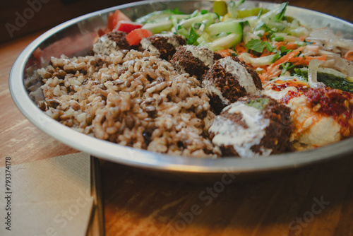 Falafel in a metallic bowl with raw fresh vegetables salad on a wooden table close up. Eating Jewish cuisine at a vegetarian cafe. Street macro food.