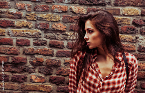 Beautiful brunette woman enjoying and standing on the old brick wall building background in casual red shirt on the spring city. Closeup vintage portrait of model.