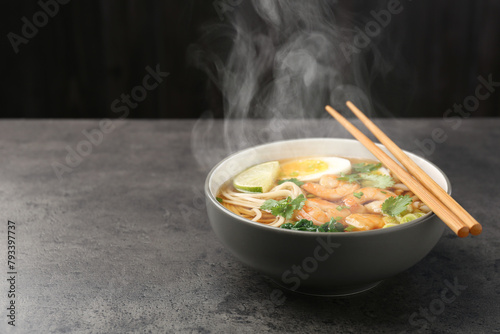 Delicious hot ramen with shrimps and chopsticks on grey table, space for text. Noodle soup