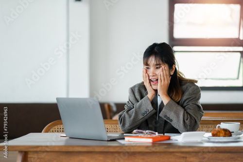 A woman is sitting at a desk with a laptop and a plate of food