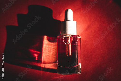 Mockup of glass cosmetic pipette bottle lying on red surface top view. Contrasting shadow of serum bottle on a table. Female daily beauty routine.