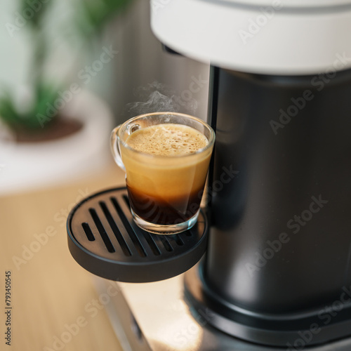 Espresso cup with steam and froth during Coffee making Coffee by Coffee Maker Machine on wood table bar. Cafe shop, Daily beverage drink at Home, Apartment and Office concept