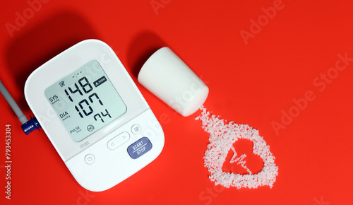 Electronic blood pressure gauge and electrocardiogram-shaped salt on a red background. Eating salt can increase high blood pressure and heart disease. photo