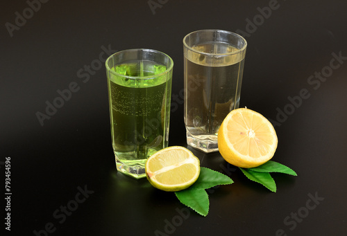 Two glasses with different citrus juices on a black background, next to slices of lemon and lime with leaves.